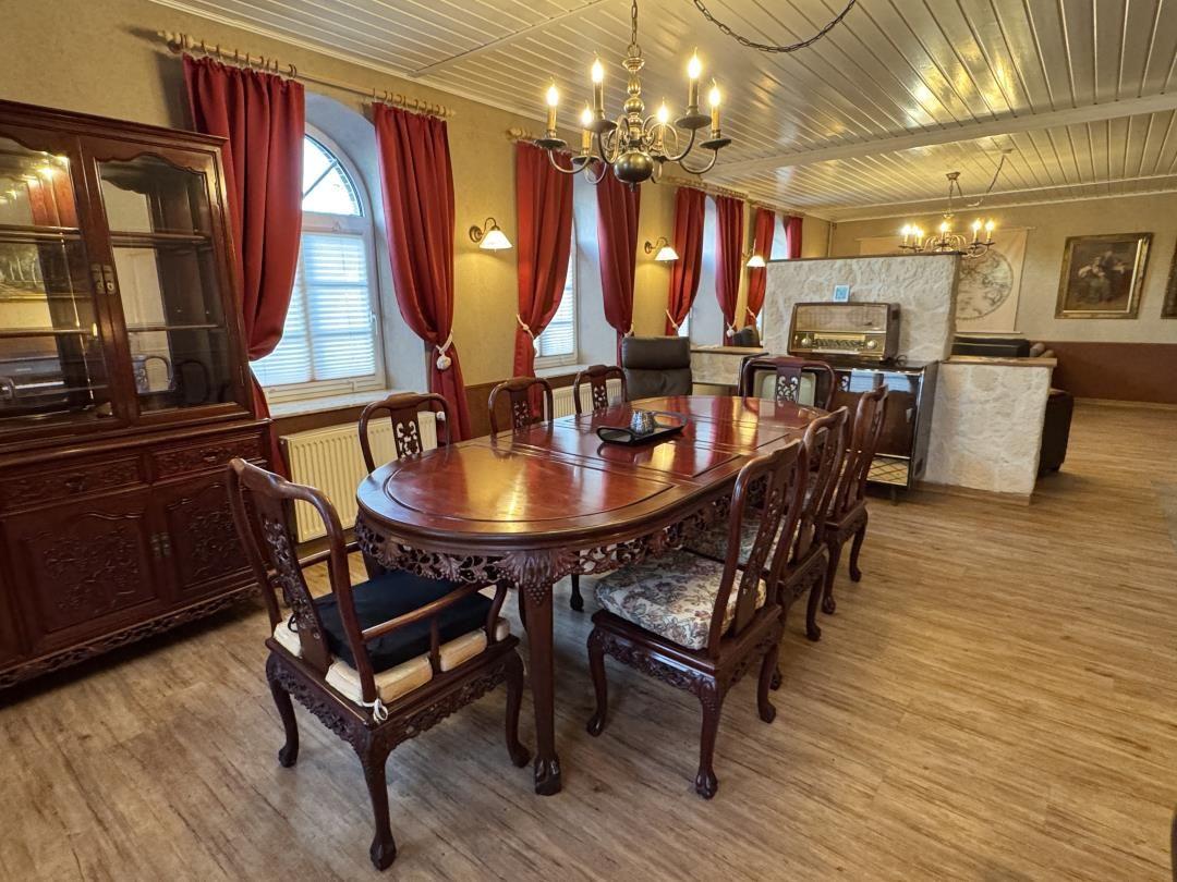 Esszimmer mit Holztisch, Stühlen und roten Vorhängen an den Fenstern.