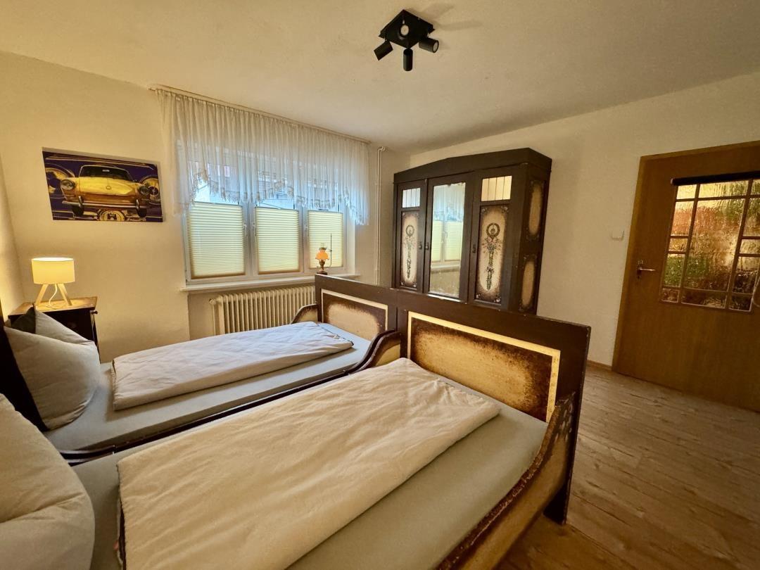 Zwei Betten, Schrank, Fenster mit Jalousien und Tür mit Glasfenstern.