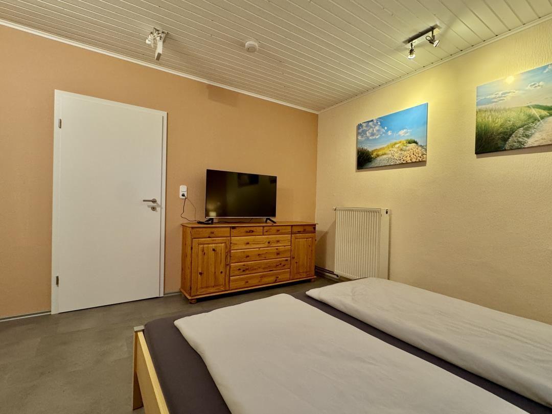 Schlafzimmer mit Doppelbett, Holzschrank und Fernseher an der Wand.