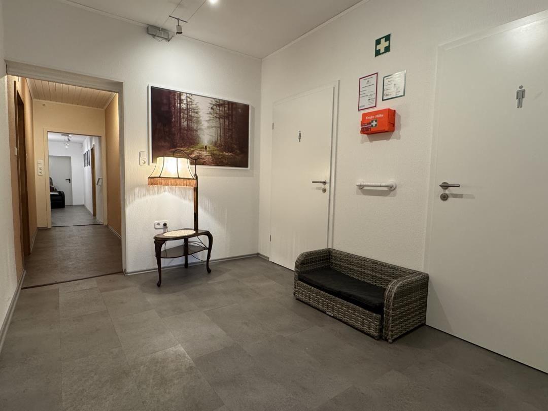 Flur mit Sitzbank, Lampenstand und Wandbild. Türen zu Badezimmern und weiteren Räumen.