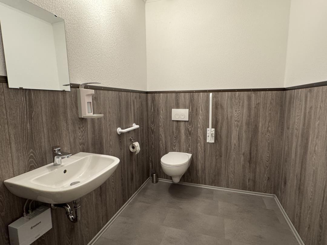 Badezimmer mit Toilette, Waschbecken und Spiegel an Holzwandverkleidung.