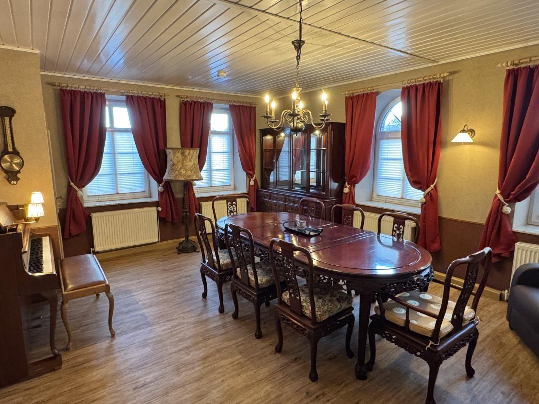 Esszimmer mit Holztisch, Stühlen, roten Vorhängen und Kronleuchter.