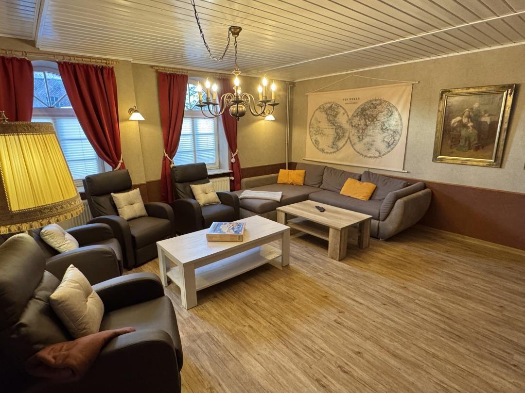 Wohnzimmer mit Sofa, Sesseln, Tisch und Wandkarte.