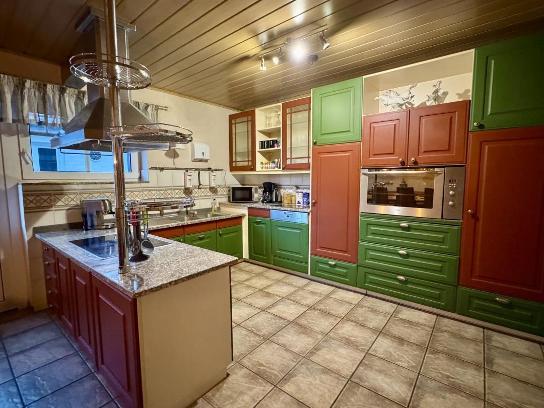 Küche mit grünen und roten Schränken, Edelstahlgeräten und Steinarbeitsplatten.
