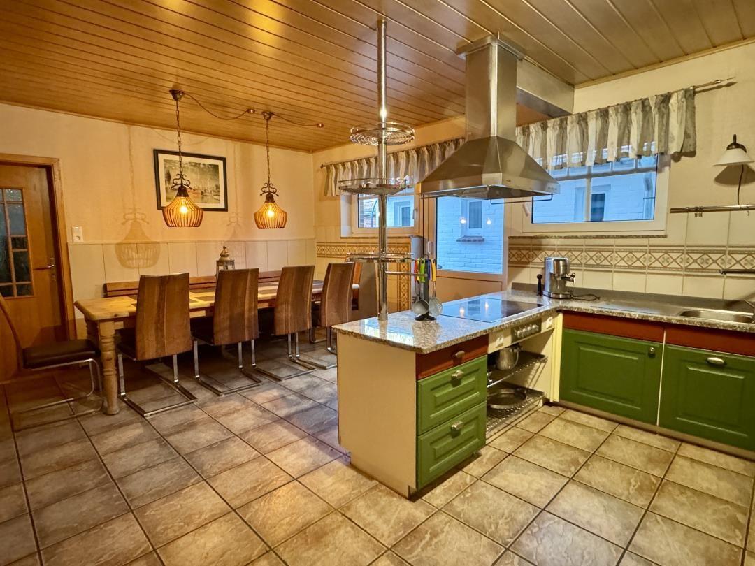 Küche mit Essbereich, grünen Schränken und Steinplatten.