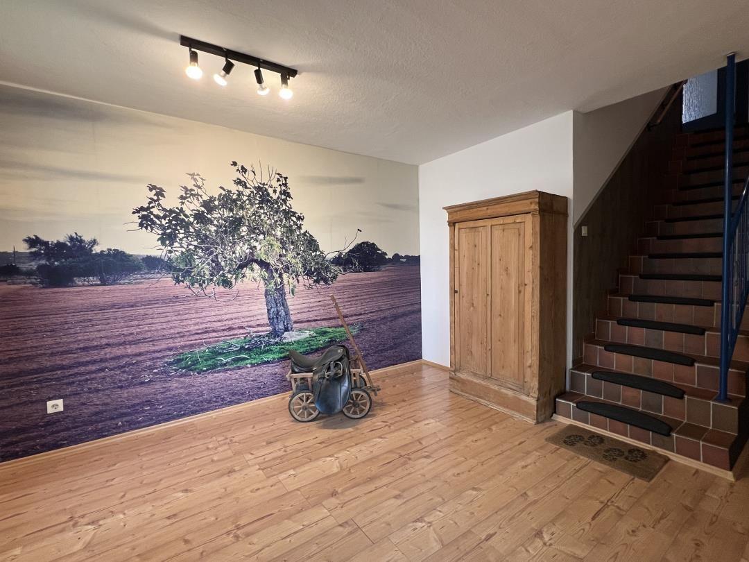 Eingangsbereich mit Holzboden, Wandbild, Holzschrank und Treppe.