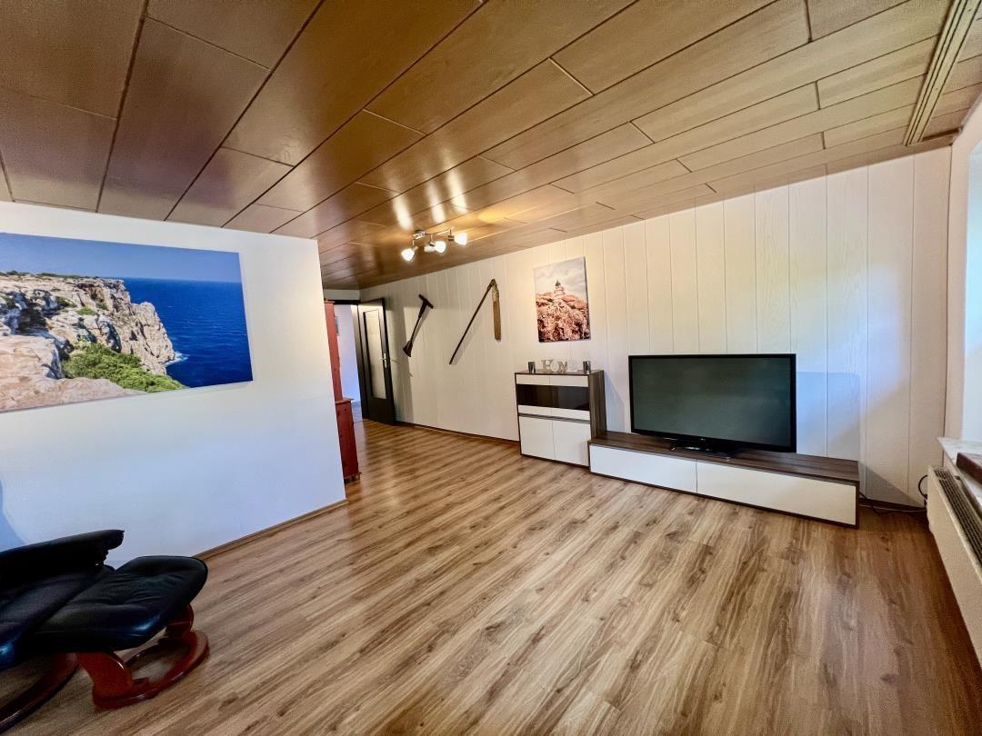 Wohnzimmer mit Holzboden, Fernseher und Wandbildern