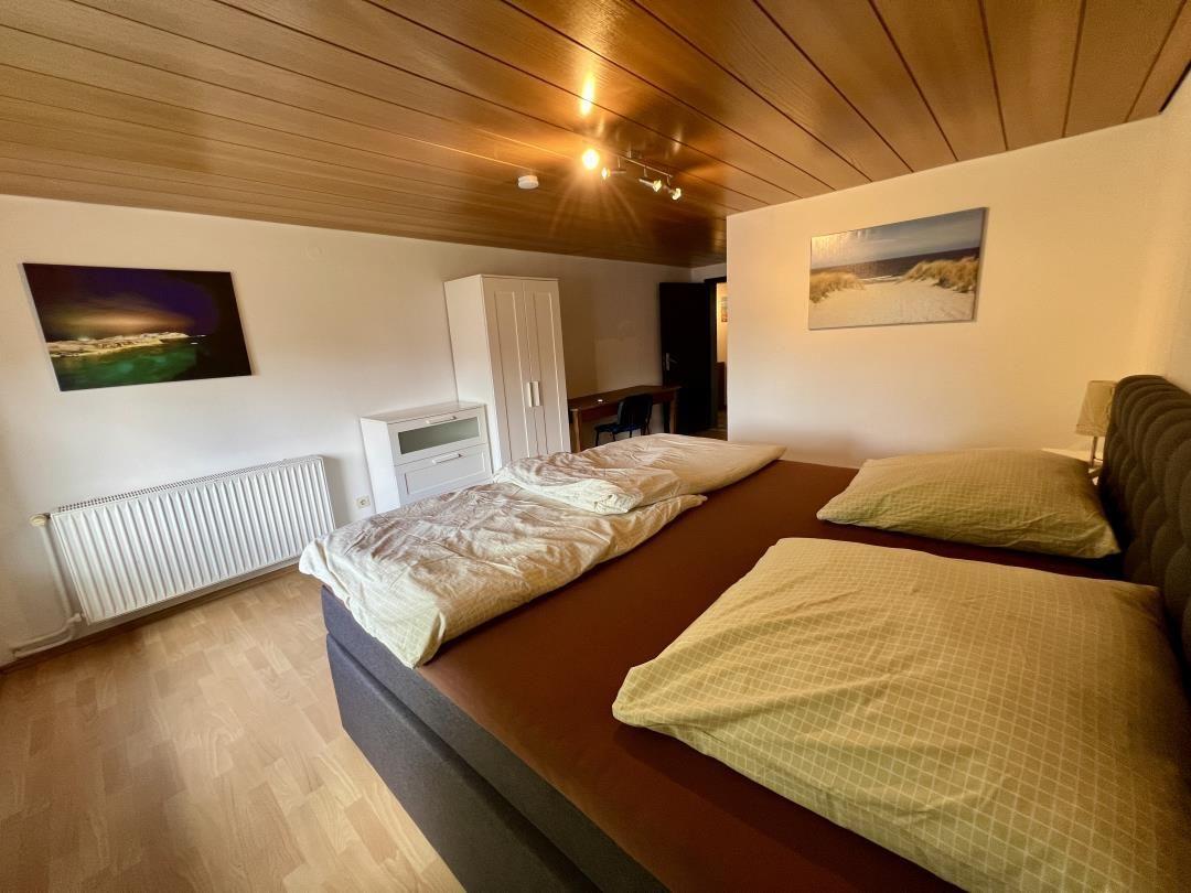 Schlafzimmer mit Doppelbett, Holzboden und Decke. Wandbild und Schrank sind sichtbar.