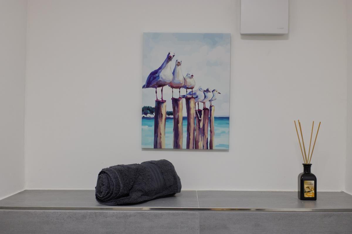 Ein Bild mit Möwen auf Pfählen hängt an der Wand. Ein Handtuch und ein Duftdiffusor stehen auf einer Bank.