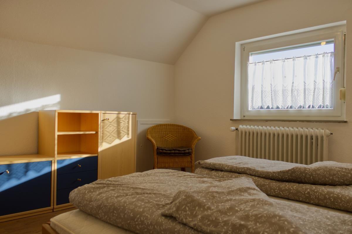 Ein Schlafzimmer mit Doppelbett, Schrank und Stuhl neben dem Fenster.