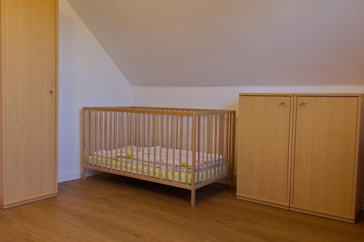 Kinderzimmer mit Holzkrippe, Kleiderschrank und Holzboden unter schräger Decke.