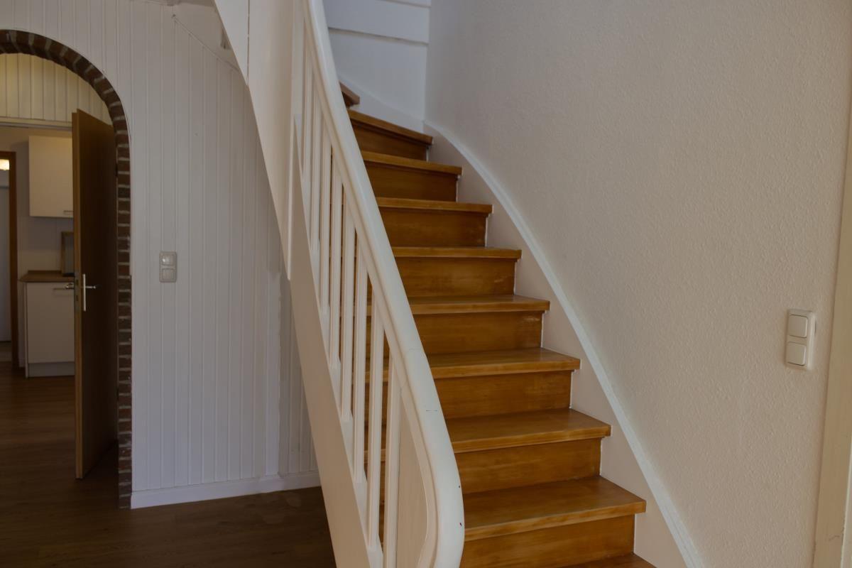 Holzgetreppe mit weißer Balustrade führt zur oberen Etage. Links ist eine Tür zum Wohnbereich.