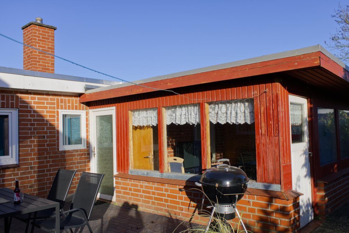 Roter Holzsaal mit Fenstern und Grill auf Terrasse. Neben einem Backsteinhaus.