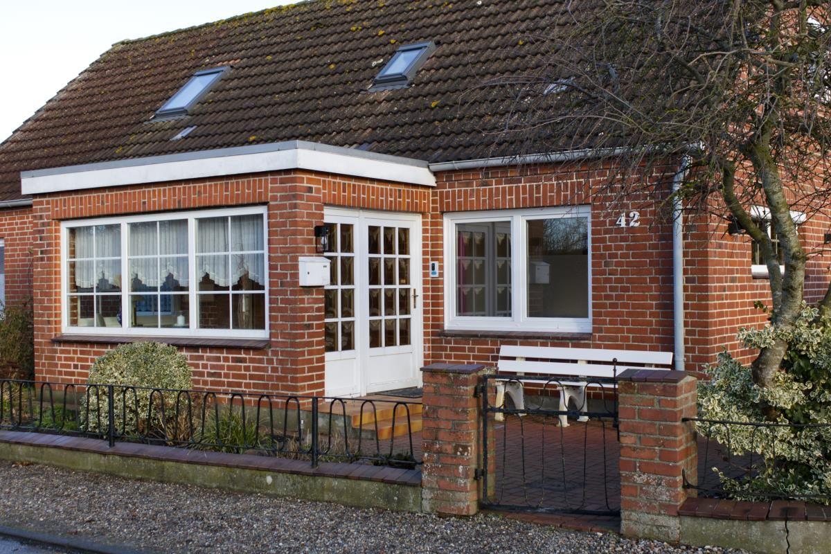 Rotes Backsteingebäude mit weißer Tür und Fenstern, Dach mit Dachfenstern, kleine Vorgärtnereingang.