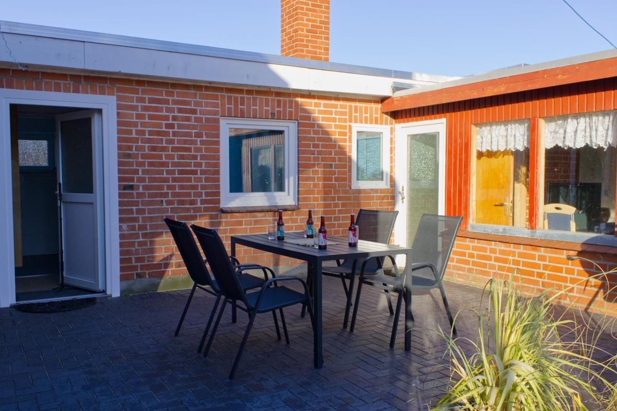 Terrasse mit Tisch und Stühlen vor rotem Backsteinhaus mit Fenstern und Tür.