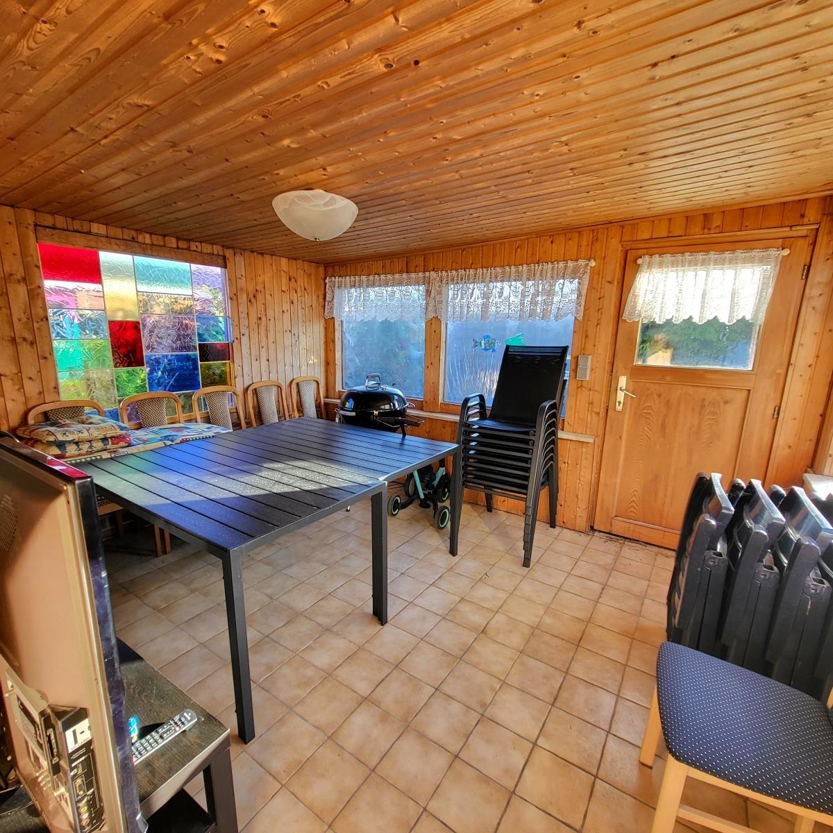 Helle Holzvertäfelung, große Fenster, Tisch mit Stühlen, Grill und Tür