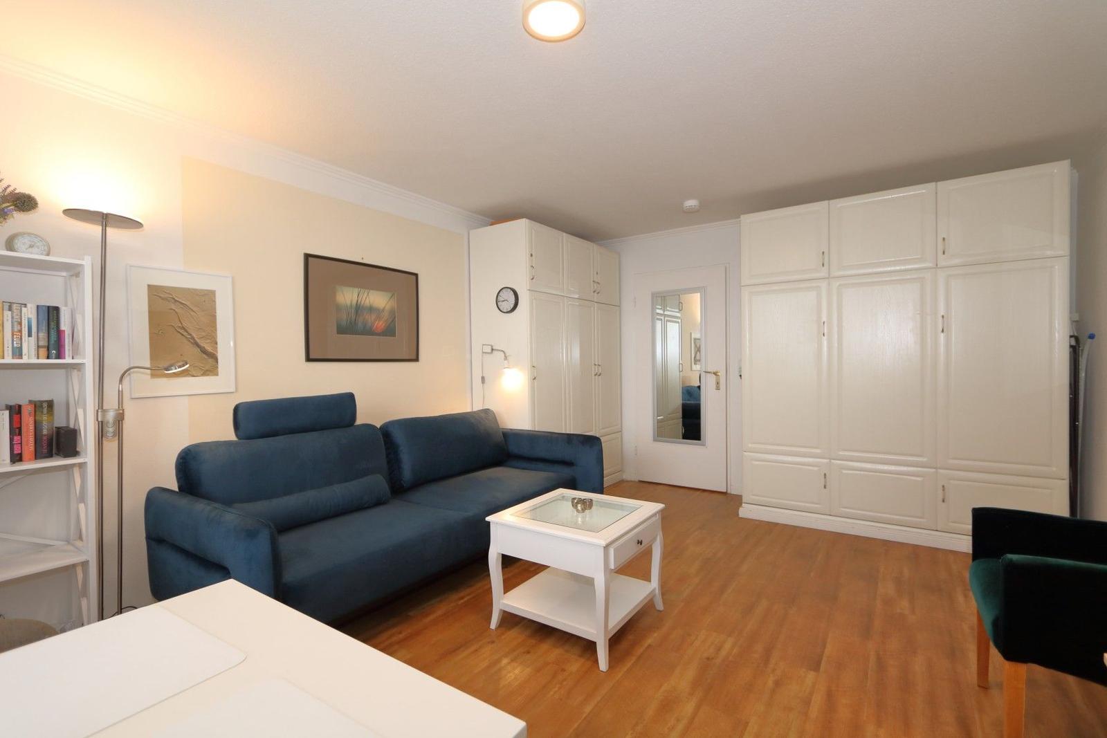 Wohnzimmer mit blauem Sofa, weißen Schränken und Holzboden.