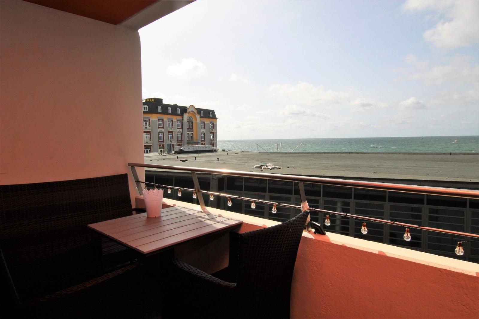 Terrasse mit Tisch und Stühlen, Blick auf Meer und Gebäude.