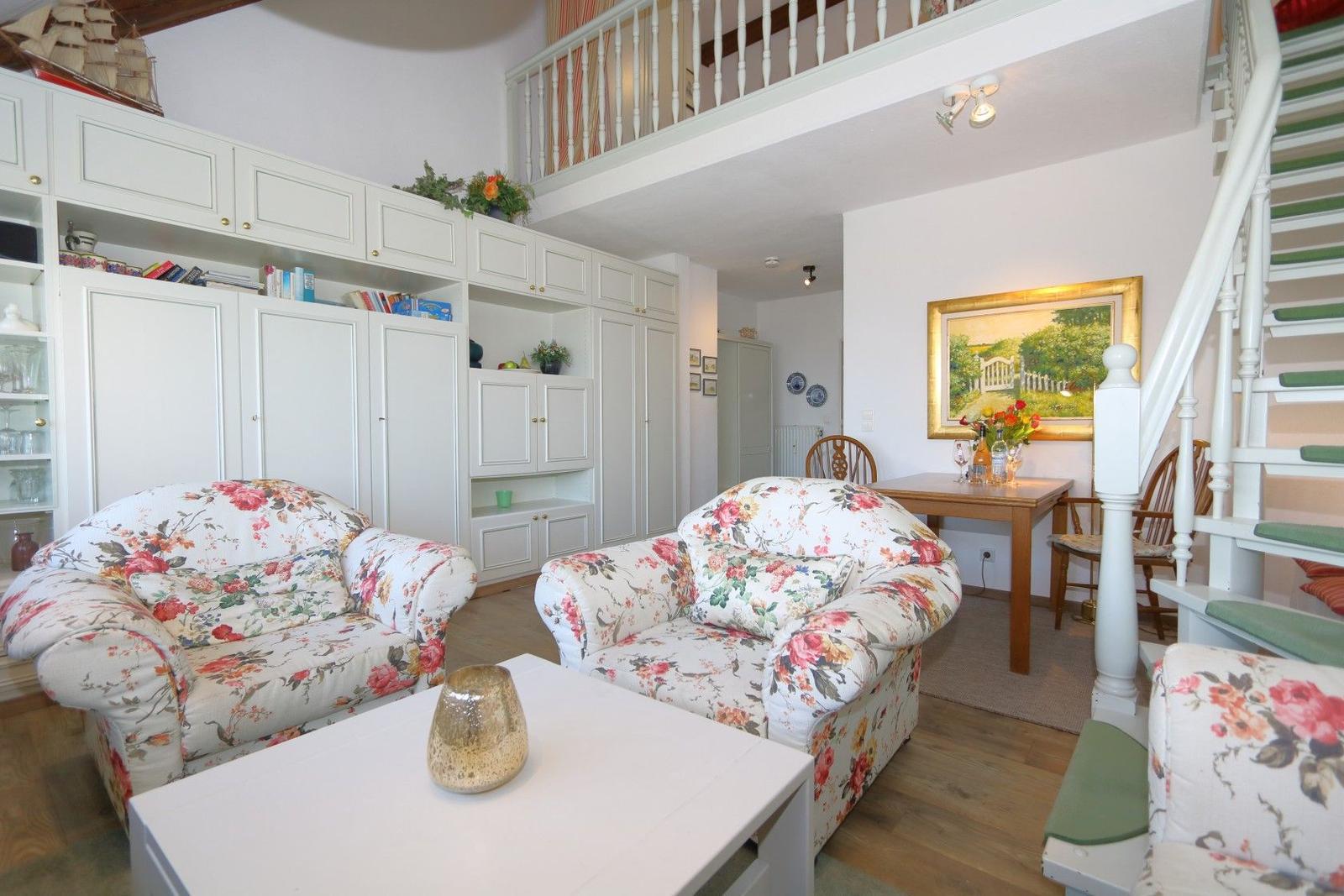 Living and dining area with floral chairs, white cabinets, and staircase to gallery.