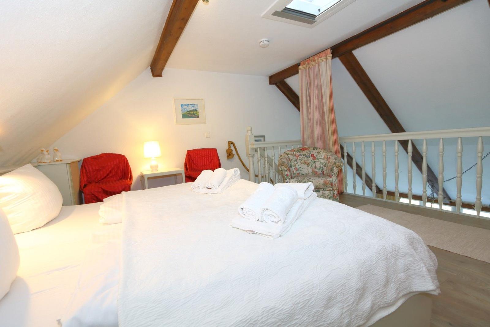 Bedroom with sloped ceiling, bed, two red chairs, and one armchair.