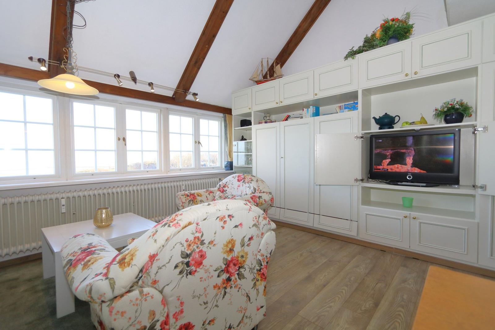 Living room with floral chairs, white cabinets, and wooden beam ceiling.