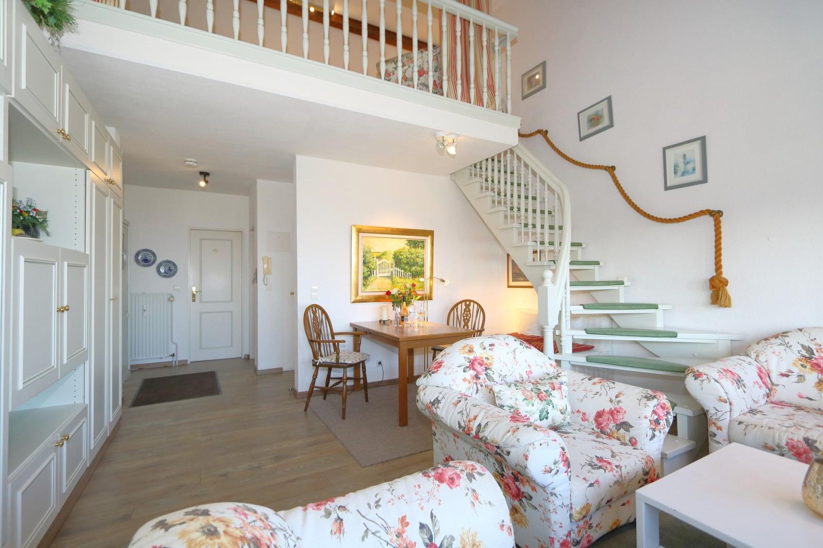 Living area with staircase and floral seating. Dining area with table and chairs.