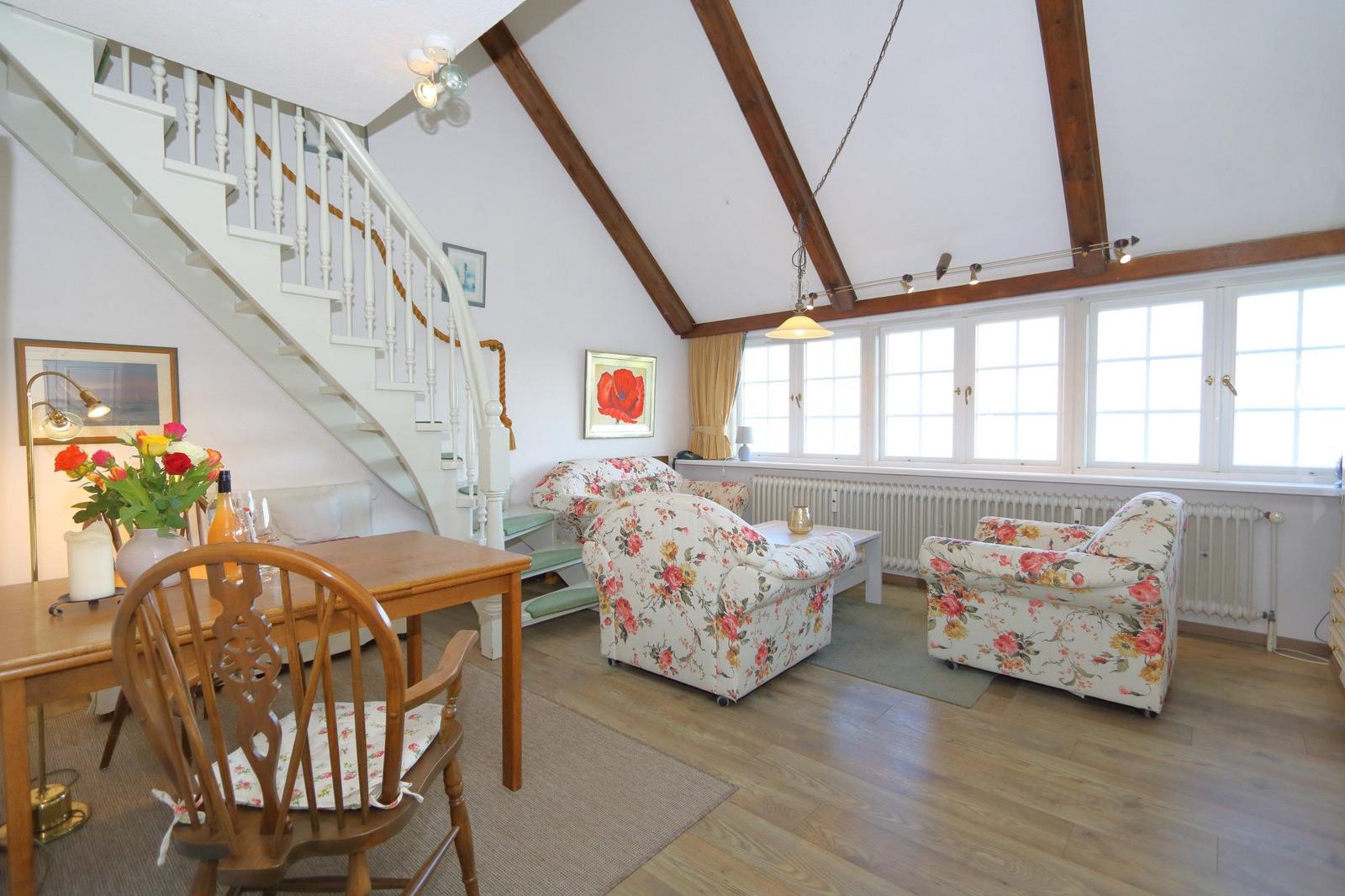 Living and dining area with hardwood floors, staircase, and floral armchairs.