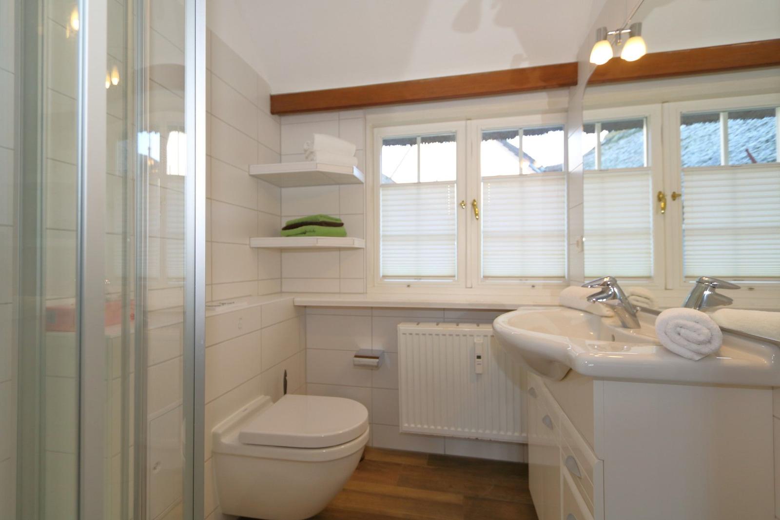 Bathroom with shower, sink and toilet. Window with blinds and wooden beam.