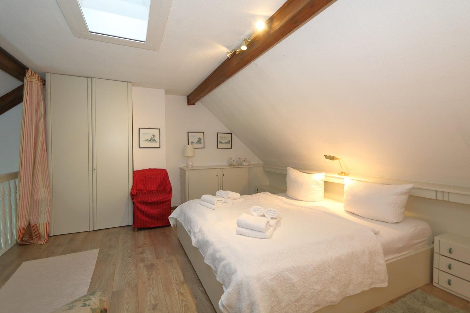 Attic room with bed, wardrobe, and sloped ceiling. Skylight and lamps provide light.