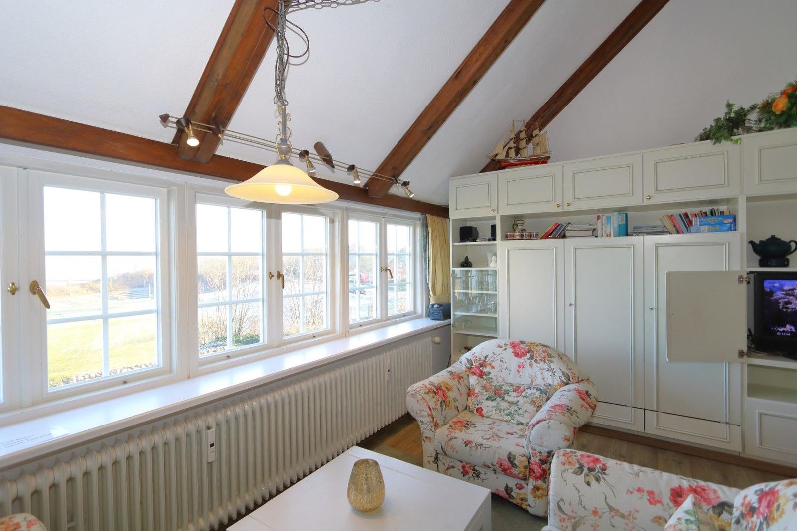 Living room with wooden beams, window front, and floral seating.