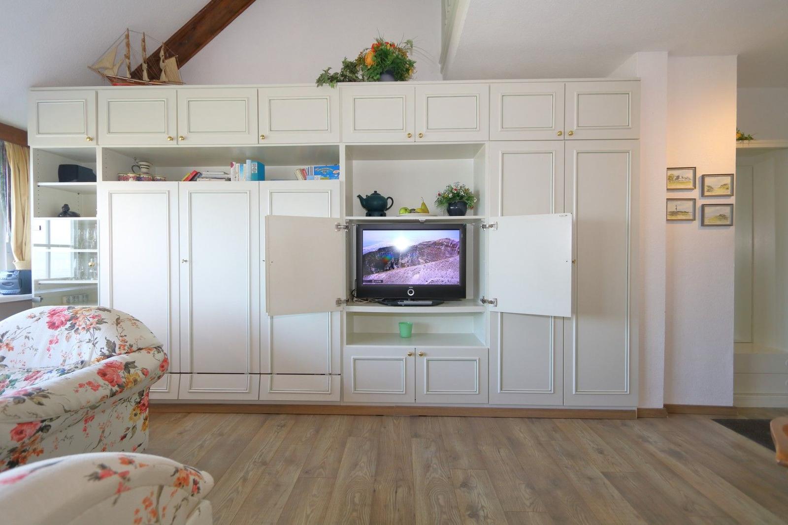 Living room with white cabinet, TV, and floral armchairs.