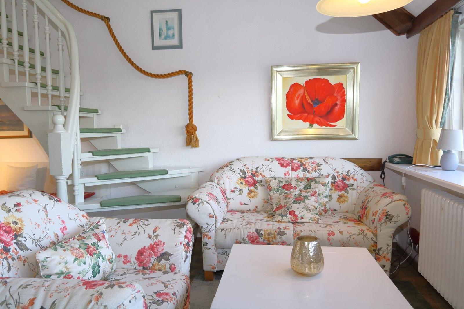 Living room with floral sofas, staircase, and wall painting of a red poppy.