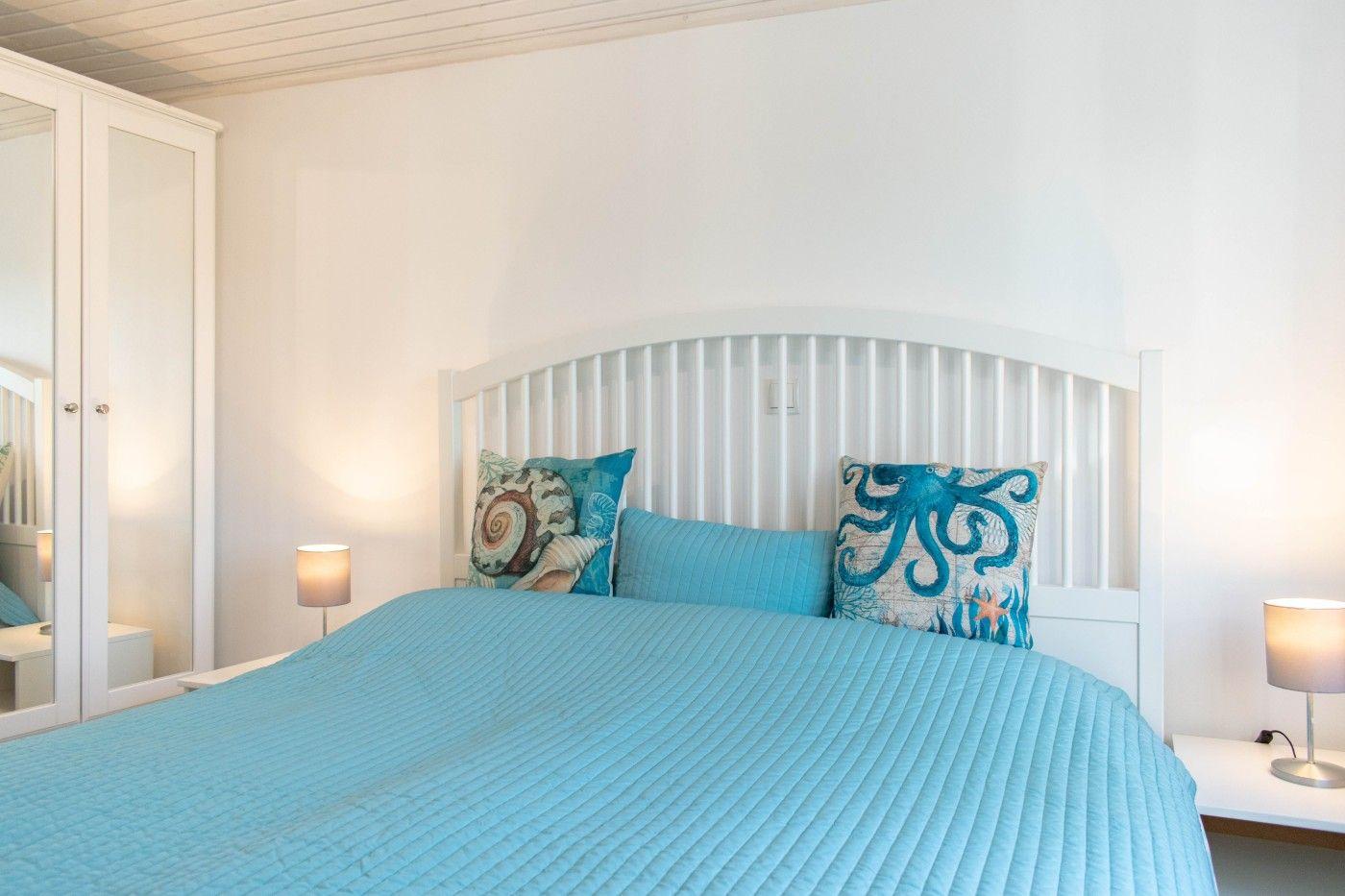 Ein Schlafzimmer mit weißem Bett und blauer Bettwäsche. An den Wänden hängen zwei Nachttische mit Lampen.