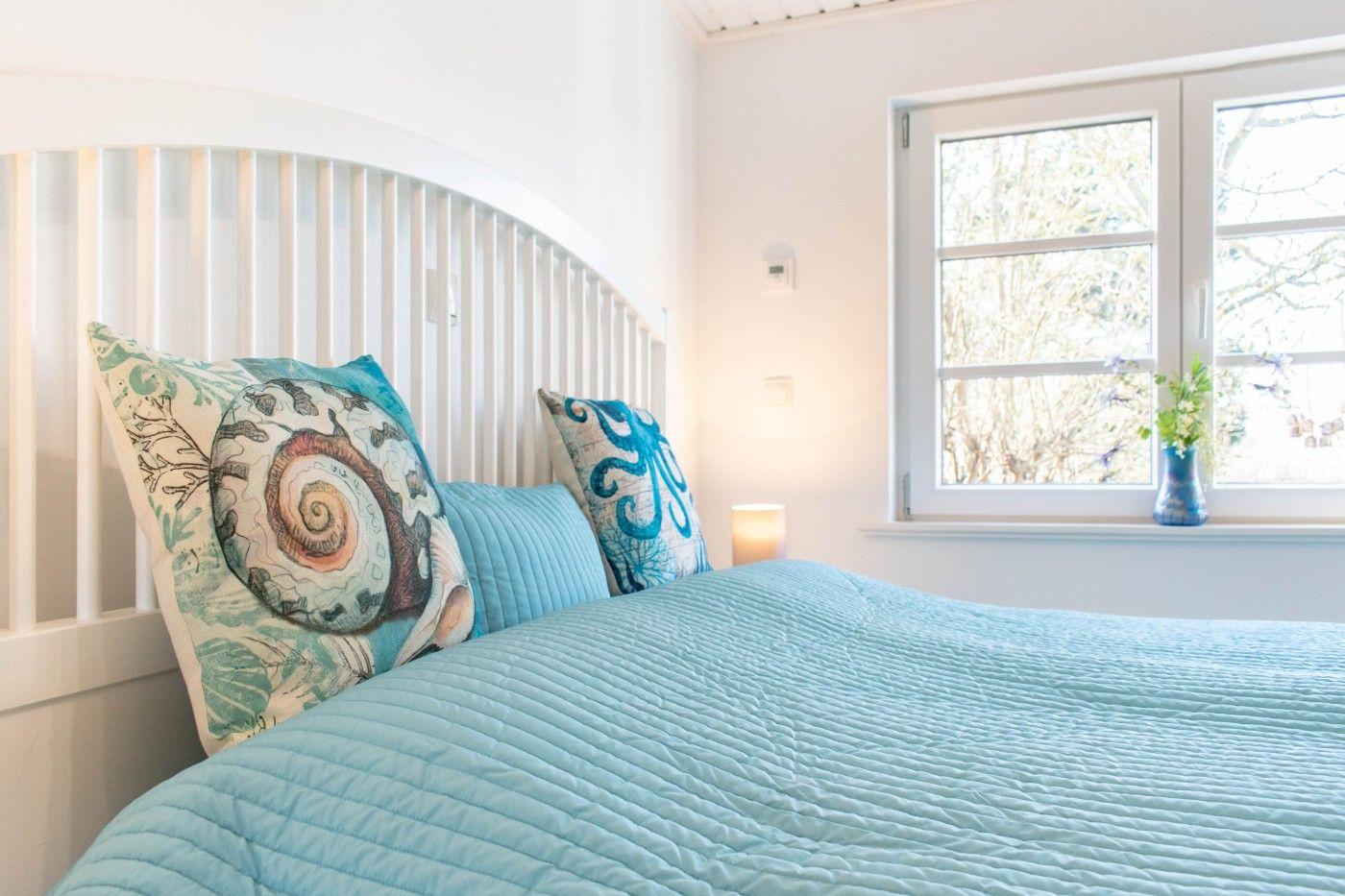Schlafzimmer mit Bett, Kissen und Fenster. Blaue Bettwäsche und Wanddekoration.