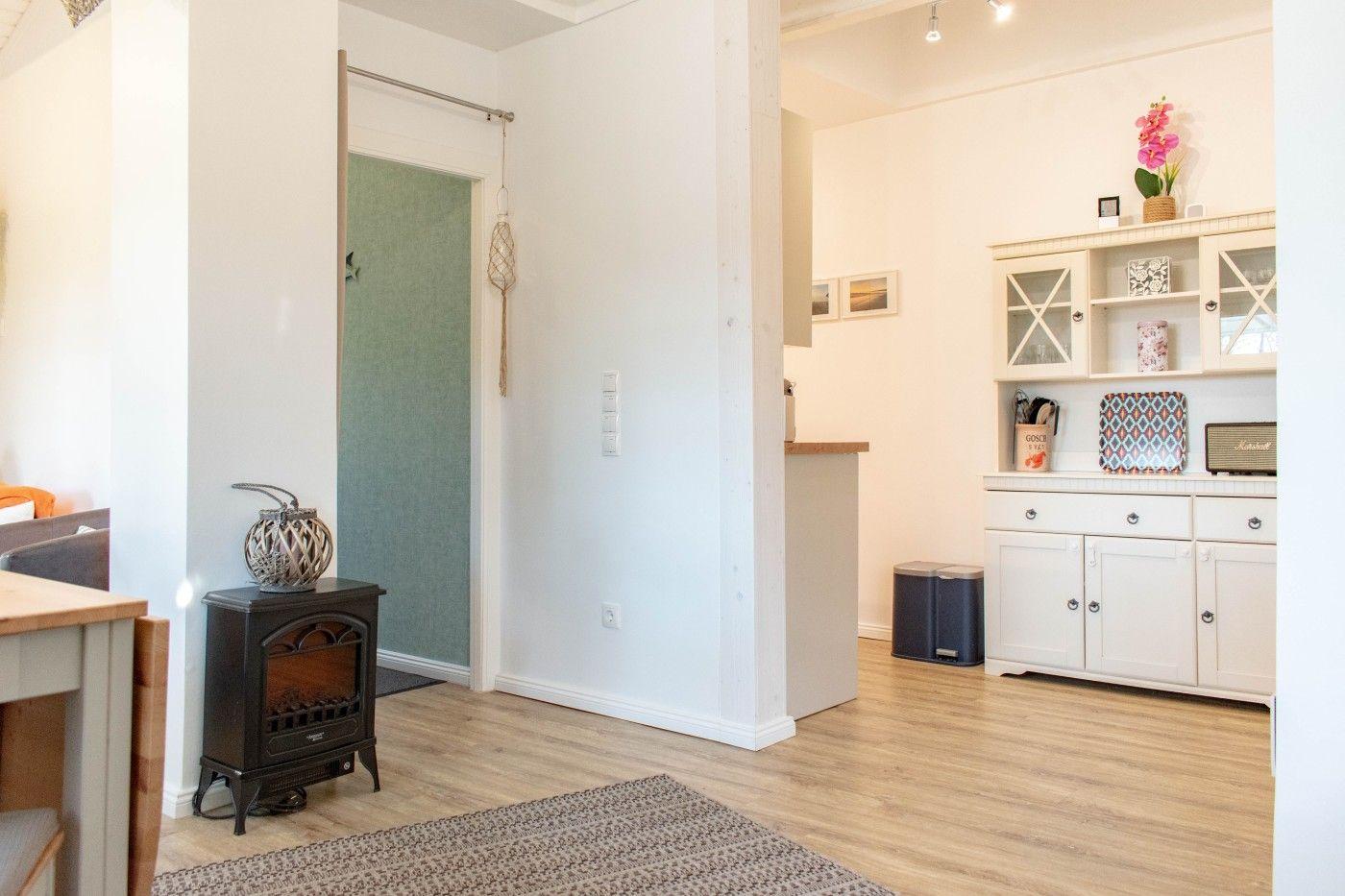 Eingangsbereich mit Holzboden, Schrank und Kaminofen. Tür zur Küche sichtbar.