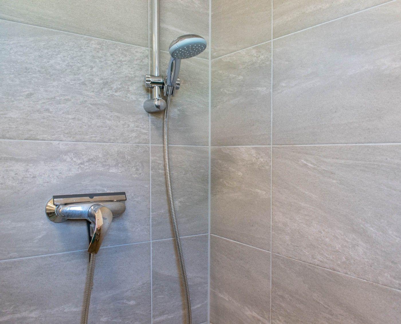 Duschbereich mit Handbrause und Wandhahn an grauen Fliesen