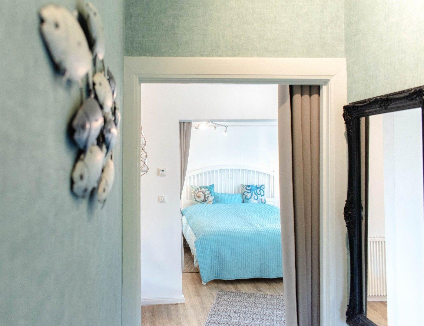 Schlafzimmer mit blauem Bett und Fensterblick. Wanddekoration und Spiegel sichtbar.