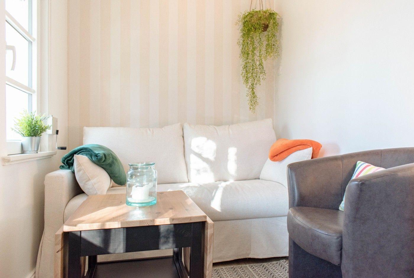 Ein Wohnzimmer mit weißem Sofa, Holztisch und hängender Pflanze.