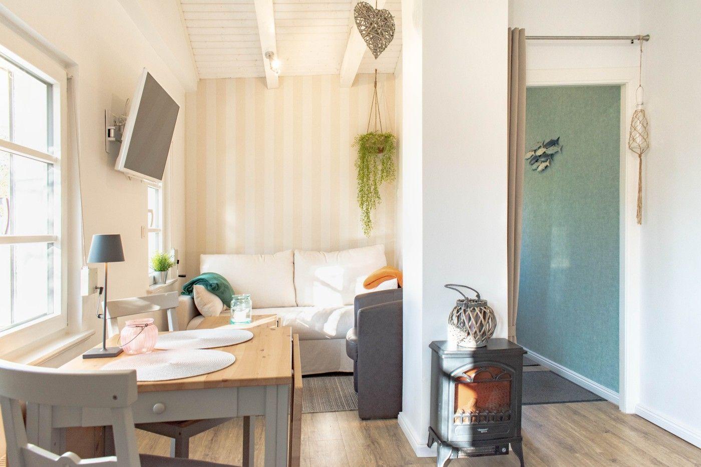 Wohnzimmer mit Sofa, Esstisch und Kaminofen. Wand mit Streifenmuster und Pflanzen.