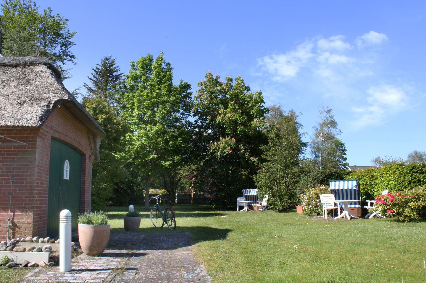 House with thatched roof, garden with sun loungers and bicycle.