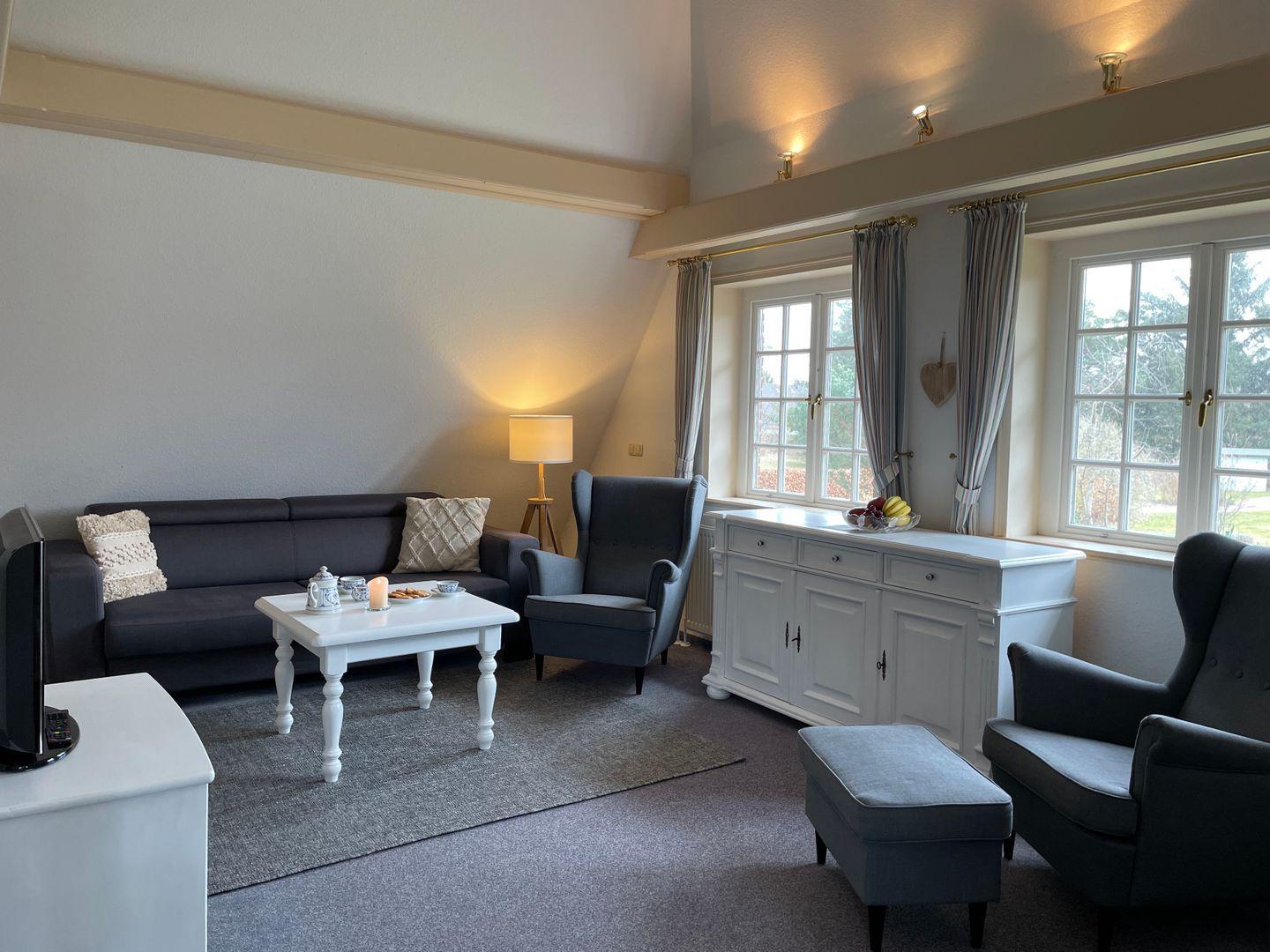 Living room with sofa, armchairs, table, and windows.