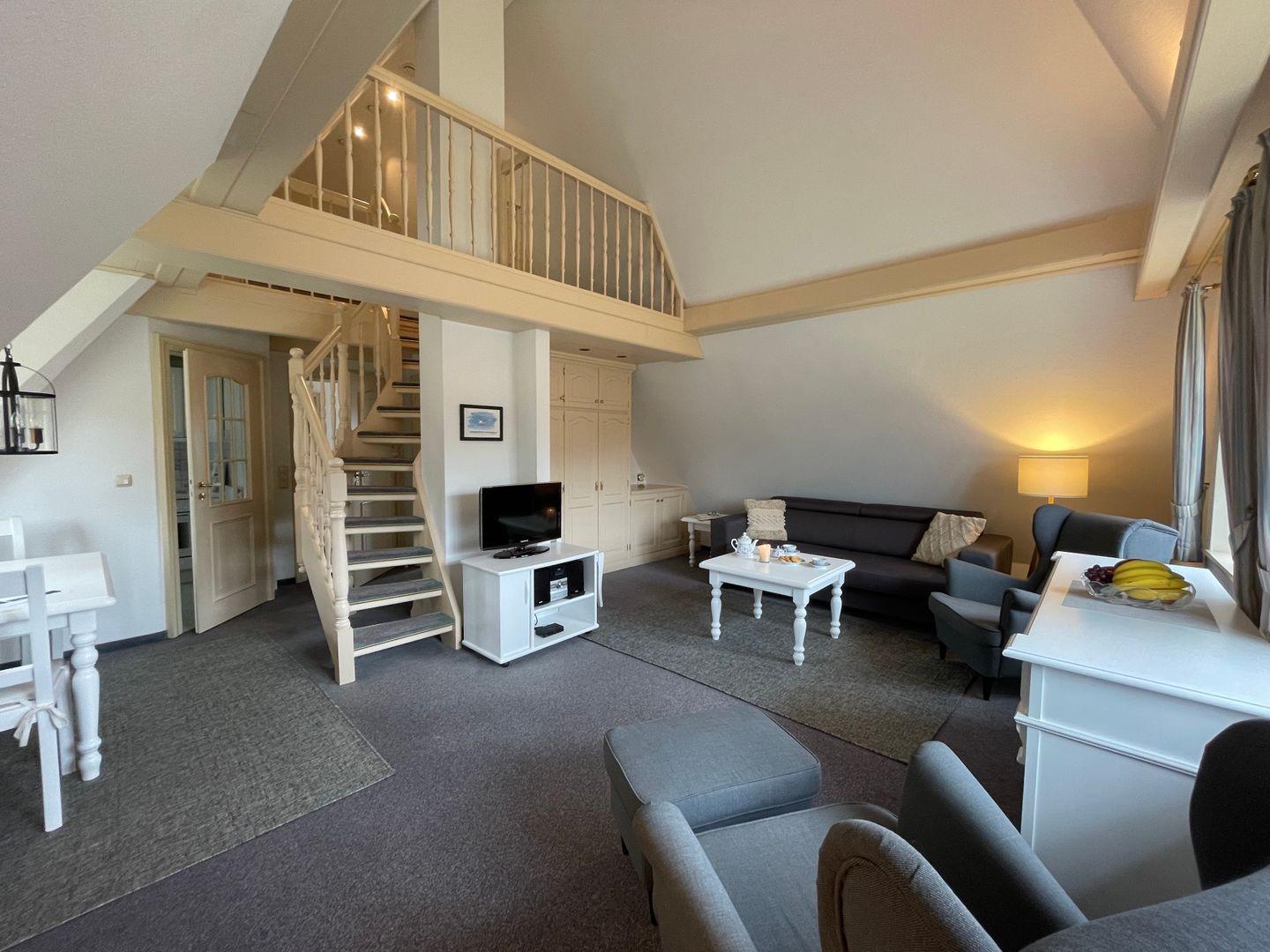 Living room with sofa, armchairs, and staircase to gallery. Dining table and TV are present.