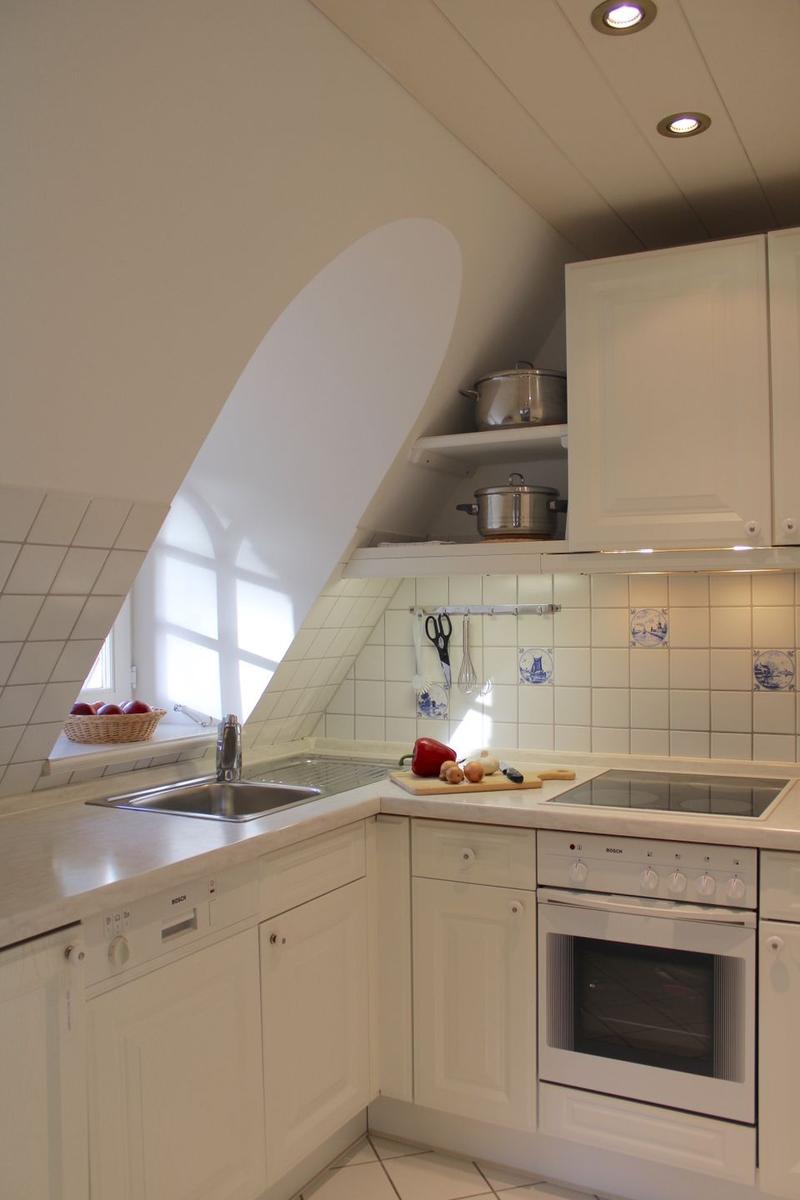 Kitchen with white cabinets, sink, stove, and oven under sloped ceiling.