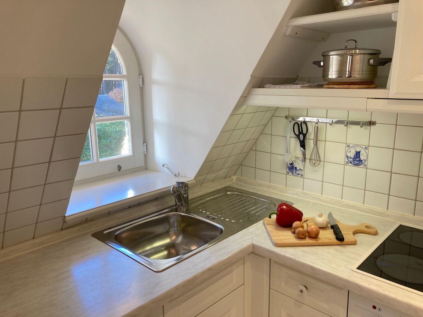 Kitchen with stainless steel sink, worktop and window. On the worktop is a wooden board with vegetables.