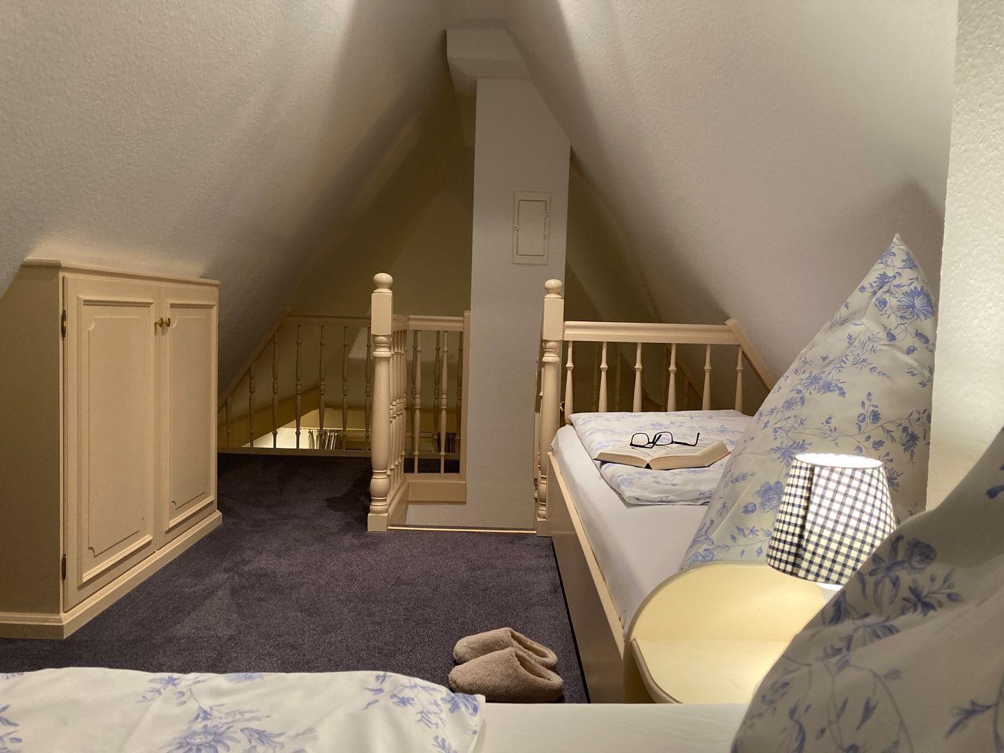 Bedroom with sloped ceiling, bed, wardrobe, and staircase.