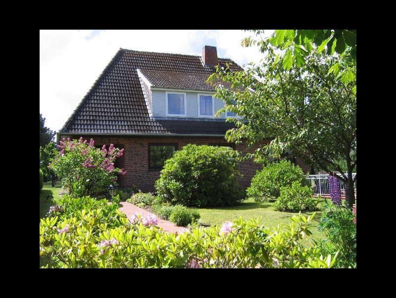 Haus mit Ziegeldach, umgeben von grünem Garten und blühenden Sträuchern.