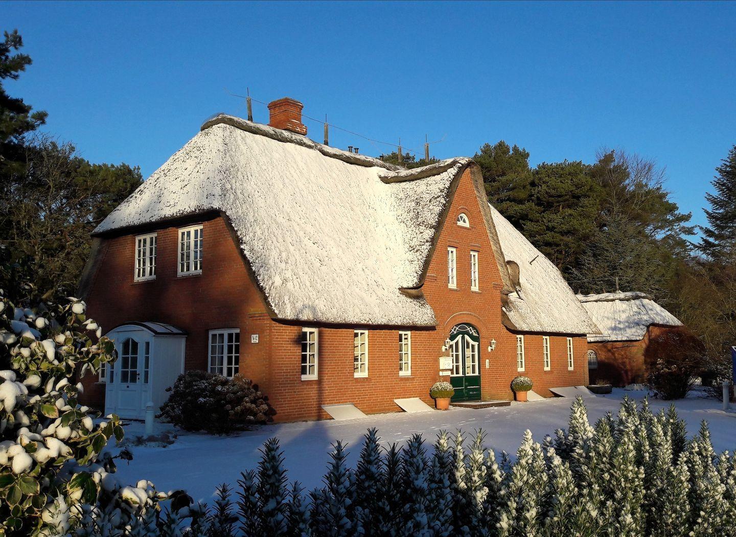 Rotes Backsteingebäude mit Schilfdecke und Schnee. Eingangstür und Fenster sind sichtbar.