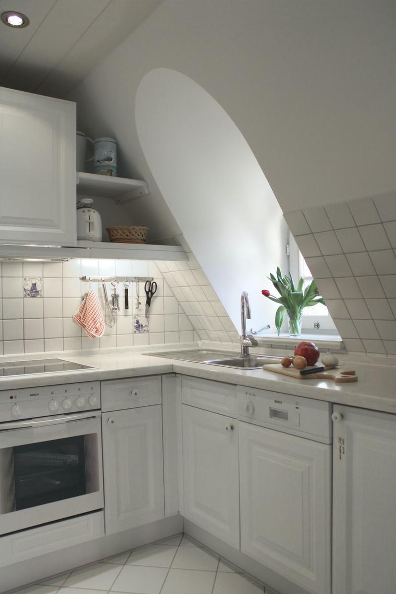 Küche mit weißen Schränken, Spüle und Herd. Dachfenster und Küchenzeile sichtbar.