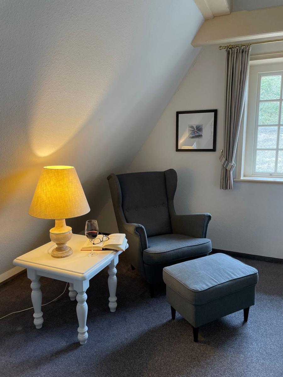 Ein Raum mit Sessel, Beistelltisch, Lampe und Fenster. Auf dem Tisch steht ein Glas Wein.