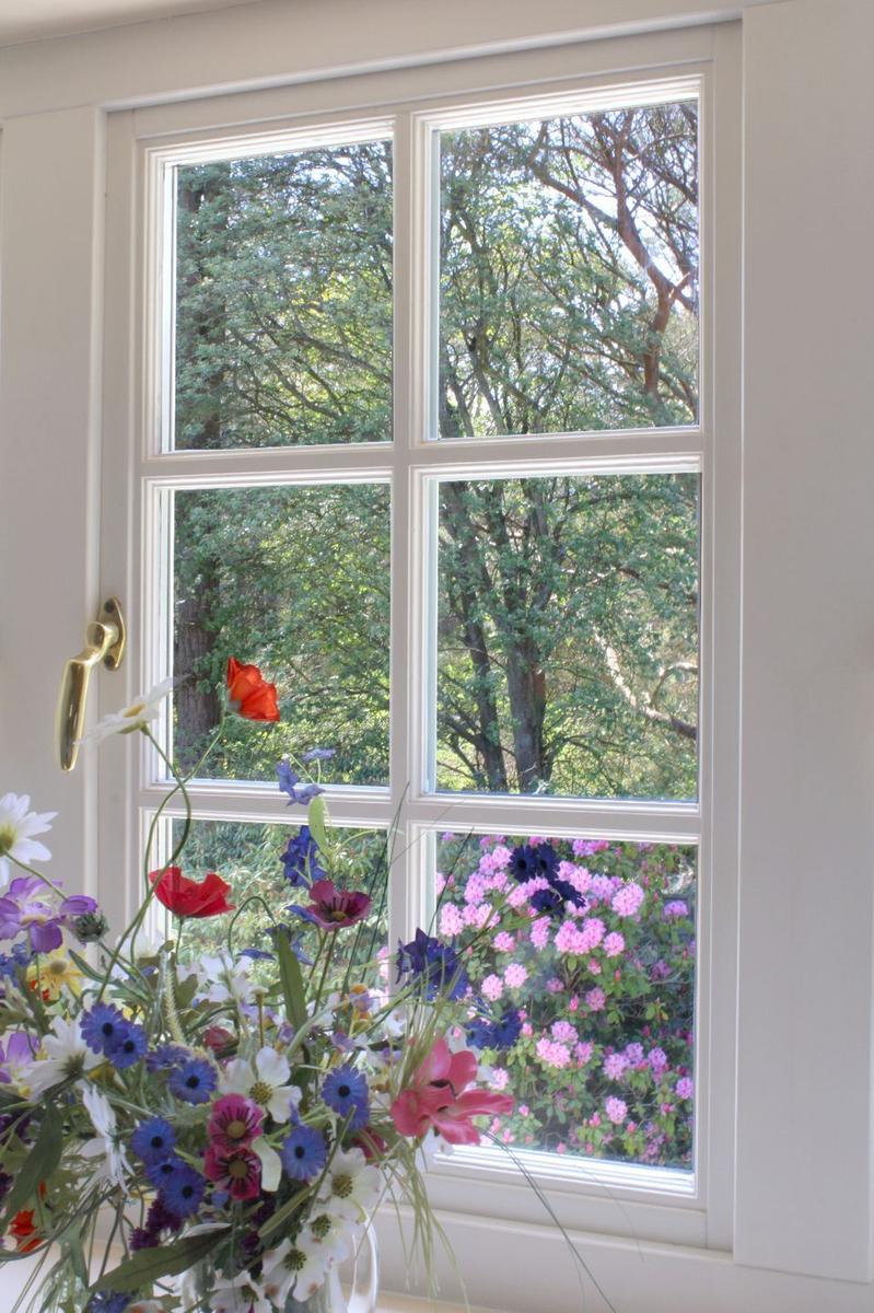 Ein Fenster mit Blumenstrauß im Vordergrund und Blick auf einen blühenden Garten.